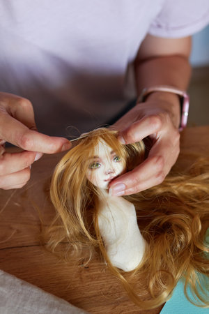 Portrait of creative young adult woman making handmade doll, sewing hair to doll.の写真素材