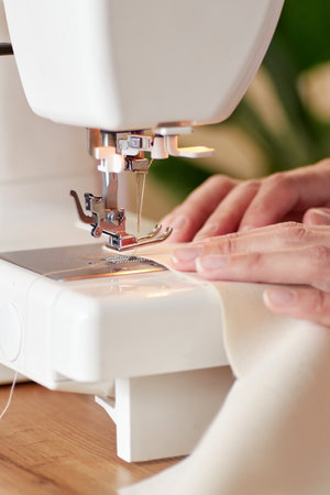 Hands of tailor woman stitching fabric using sewing machine.