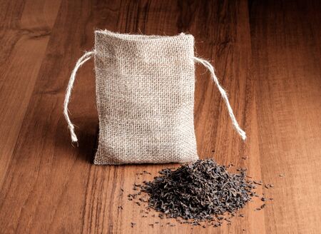 Dry black Indian tea with vintage burlap bag on wooden backgroundの写真素材