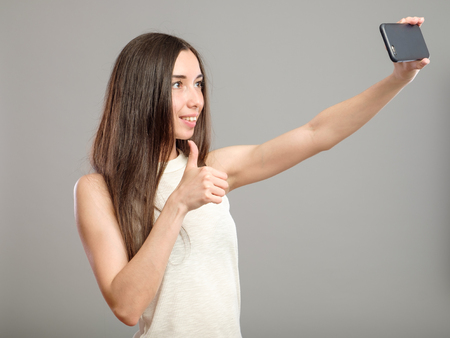 Beautiful woman taking self picture with smartphone camera isolated on grayの写真素材
