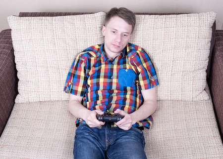 Young man playing  video games sitting at sofa and holding remote controller