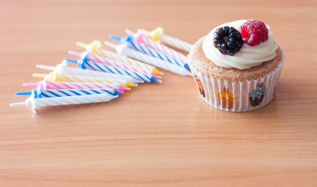 Birthday homemade cupcake with fresh raspberry, blackberry and cream  topping on wooden desk and candles on itの写真素材