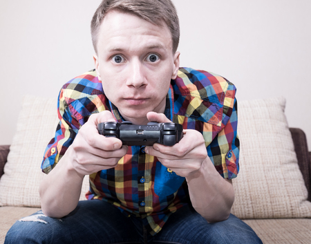 Young man playing  video games sitting at sofa and holding remote controller