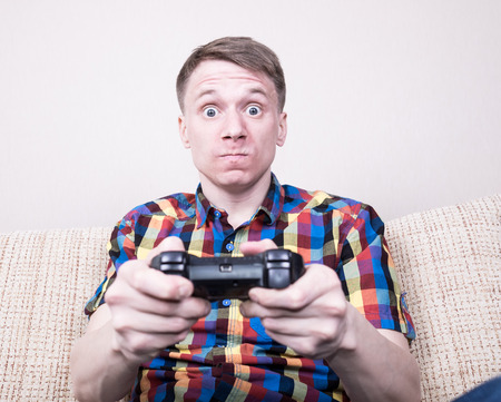 Frustrated yound man playing  video games sitting at sofa and holding remote controllerの写真素材