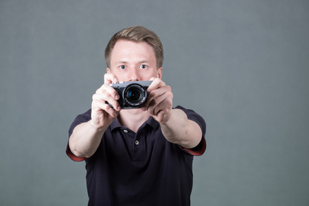 Young funny guy holding retro style camera isolated on grey backgroundの写真素材
