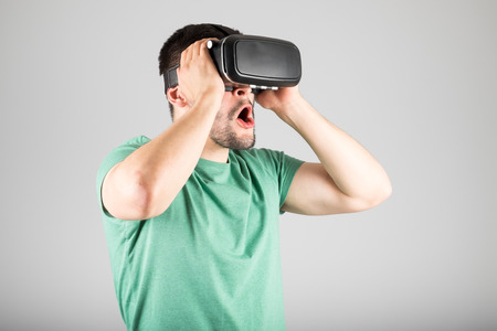 Attractive man using virtual reality headset isolated on a gray background
