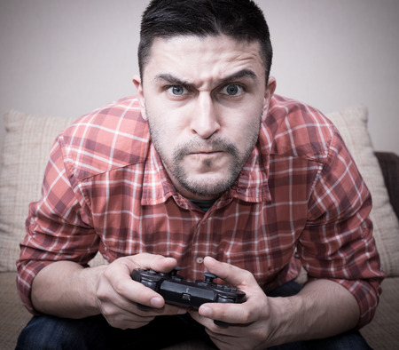 Young funny man playing  video games sitting at sofa and holding remote controllerの写真素材