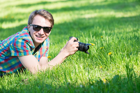 Young man in colorful shirt with digital camera shooting macro on green fresh grass in parkの写真素材