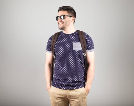 Portrait of a young man with sunglasses and backpack isolated on gray backgroundの写真素材