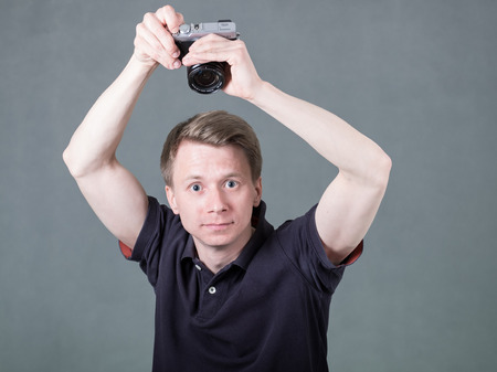 Young funny guy holding retro style camera isolated on grey background