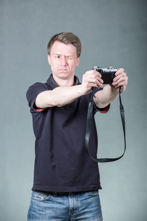 Young handsome guy taking selfie with retro style digital camera on grey backgroundの写真素材