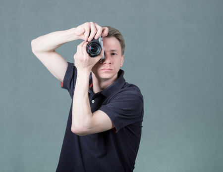 Young funny guy holding retro style camera isolated on grey background
