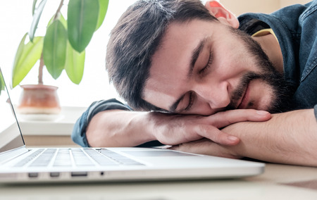 Bearded man sleeping at his working place home office with head on the deskの写真素材