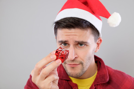 Closeup portrait unhappy, upset man holding small red box gift, disgust on face, isolated on gray background. Negative human emotion, facial expressionの写真素材
