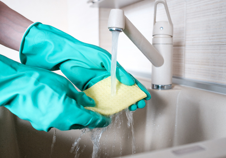 Hand in rubber glove in water stream at kitchen faucetの写真素材