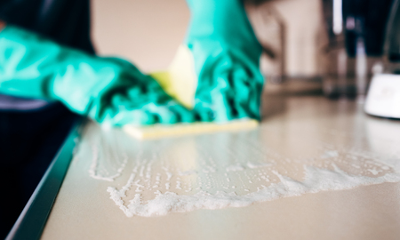 Man's hand holding a yellow rag and cleaning desk in the kitchen