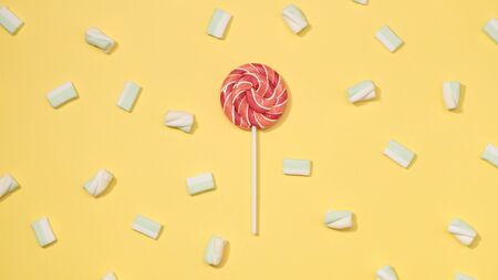 Sweet marshmallows minimalism set with red lollipop on pastel straw yellow backgroundの写真素材