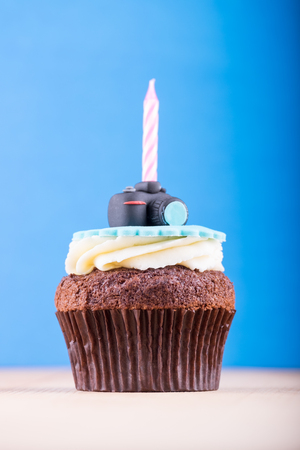 Delicious birthday cupcake with realistic camera icon on it and candle on wooden desk and blue backgroundの写真素材