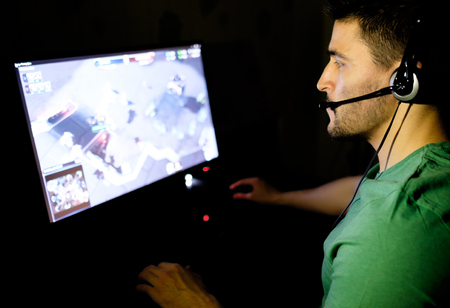Young man with headphones playing video game in dark room