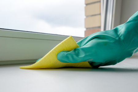 Hand in green glove cleaning windowsill with yellow clothの写真素材