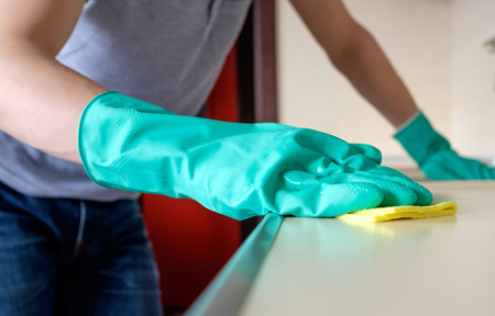 Man's hand holding a yellow rag and cleaning desk in the kitchen