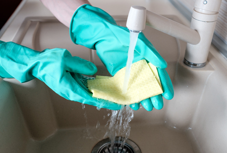 Hand in rubber glove in water stream at kitchen faucetの写真素材