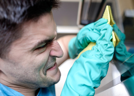 Adult man with yellow cloth in his hands which put on green rubber gloves cleaning oven with reflection on itの写真素材