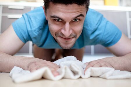 Man in blue tee manually mopping the tile floor in his house