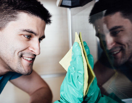 Adult man with yellow cloth in his hands which puttion on green rubber gloves cleaning oven with reflection on itの写真素材