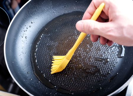 Greasing dripping pan by yellow silicone brush with olive oil