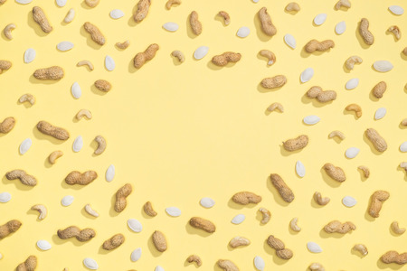 Peanut, pumpkin seeds and cashews flat lay frame on yellow background