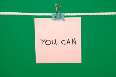 Pink paper sheet on the string with text You Can over colorful backgroundの写真素材