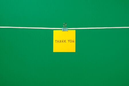 Yellow paper note on clothesline with text Thank You over colorful background