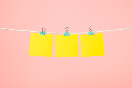 Blank yellow paper notes hanging on clothesline over pink backgroundの写真素材