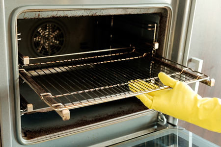 Close up of male hand with yellow protective gloves cleaning ovenの写真素材