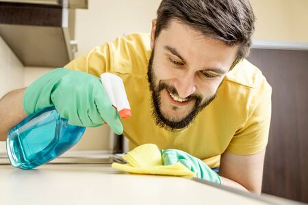Male janitor cleaning kitchen with detergent spray bottle and sponge