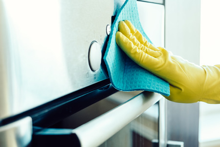 Man's hand in yellow glove cleaning the kitchen oven with rag