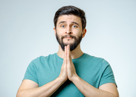 Hopeful young man praying isolated over gray