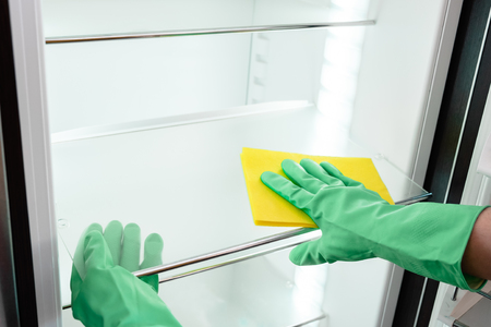 Man's hand in green rubber protective glove cleaning white opened empty refrigerator with yellow ragの写真素材