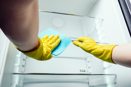 Man's hand in gloves cleaning white fridge with blue rag at kitchenの写真素材