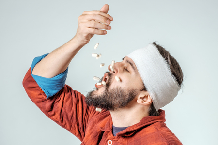 Man in medical bandage holding pills in a hand isolated on gray backgroundの写真素材