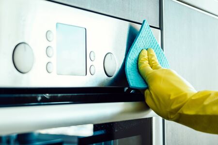 Man's hand in yellow glove cleaning the kitchen oven with ragの写真素材