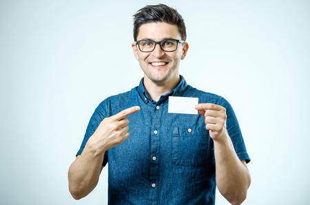 Casual young businessman holding and pointing business card. Isolated on grayの写真素材
