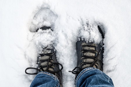 Feet in black trekking boots on snow. Winter walking. Top viewの写真素材