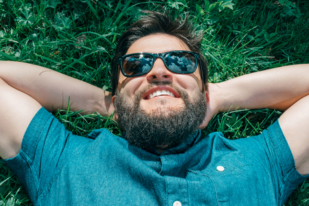 Portrait of a young happy man relaxing on the grass with his hands behind the headの写真素材