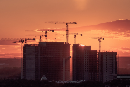Crane and building silhouettes at sunrise. Abstract Industrial background with construction cranes silhouettes over amazing sunset skyの写真素材