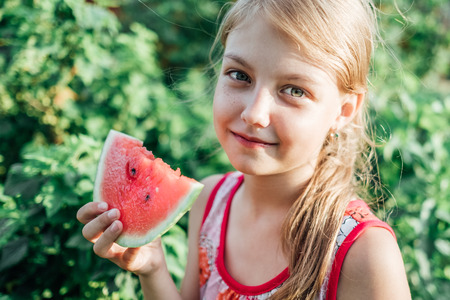 Funny portrait of adorable blonde little girl eating watermelon outdoors. Healthy fruit snack for...