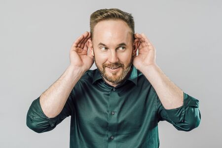 Young handsome man over isolated gray background with hand over ear listening and hearing to rumor...