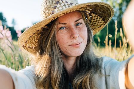Self portrait of beautiful young blonde smiling woman in straw hat on nature background in the park. Travel. Selfieの写真素材