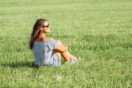 Woman wearing dress sitting on green grass field, summer seasonの写真素材